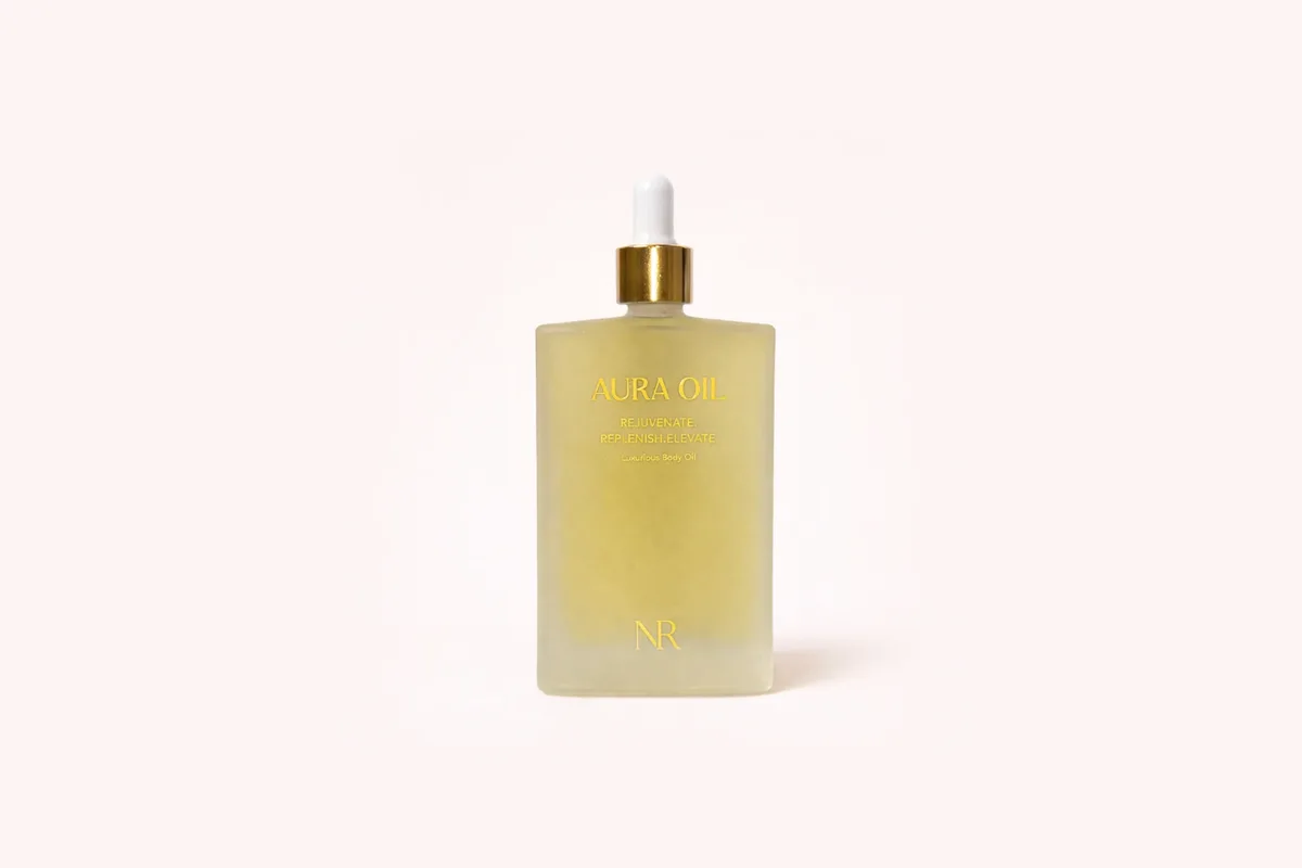A frosted glass bottle of Aura Oil with a gold dropper
